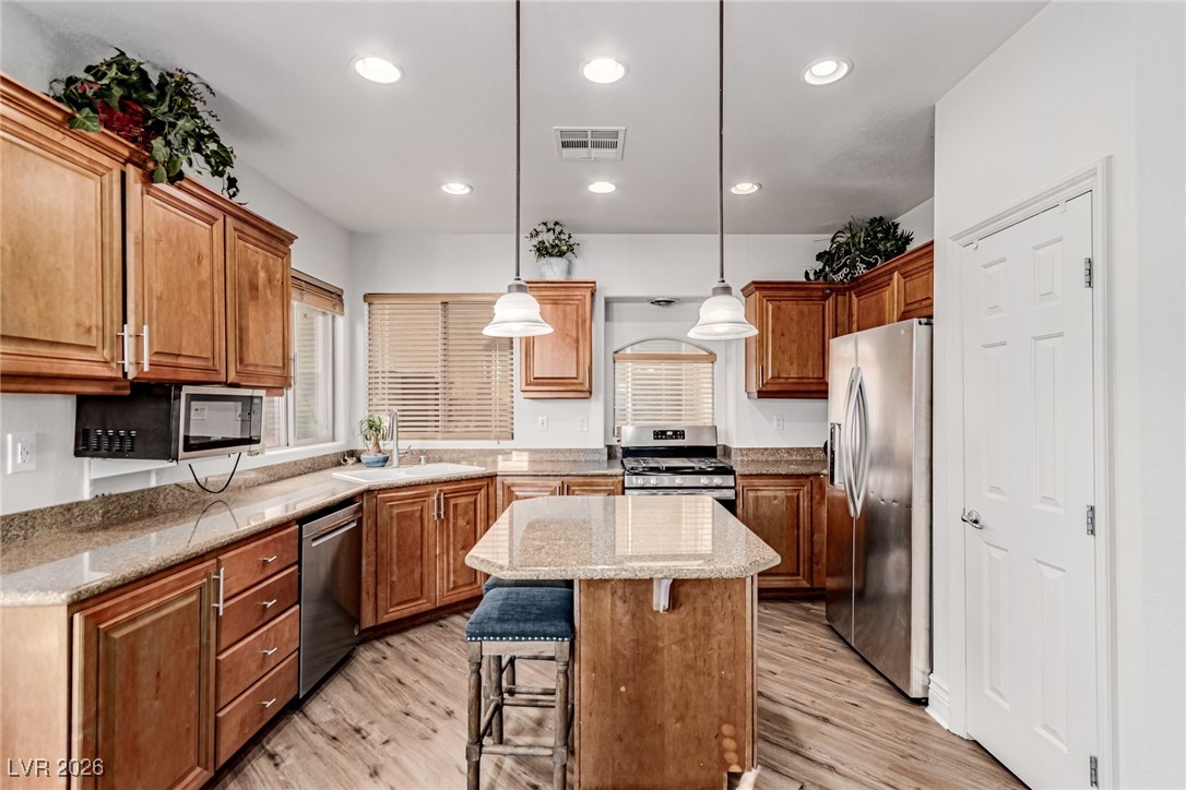 Kitchen with brown cabinets, light stone countertops, light wood-style floors, and recessed lighting