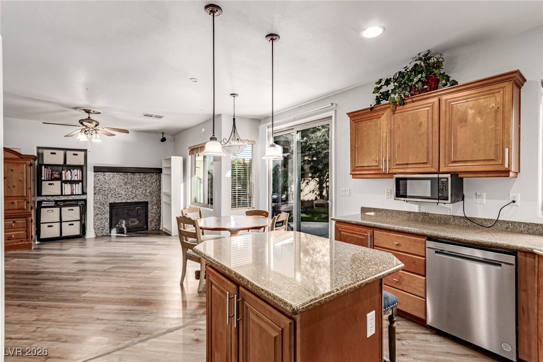 135 Broken Putter Way Las Vegas, NV 89148 - Photo 11 of 40 Kitchen featuring brown cabinets, dark stone countertops, appliances with stainless steel finishes, light wood-style floors, and a kitchen island