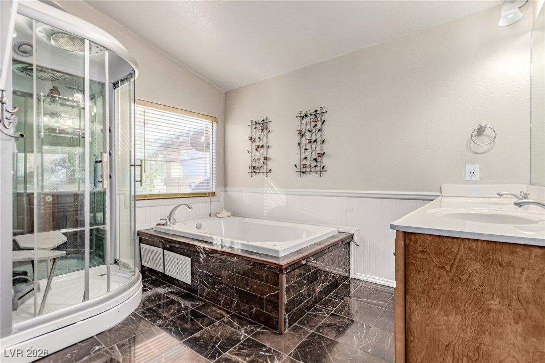 135 Broken Putter Way Las Vegas, NV 89148 - Photo 18 of 40 Bathroom featuring vaulted ceiling, double vanity, a garden tub, dark marble finish flooring, and a shower stall