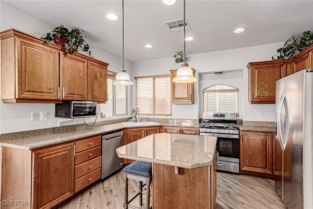 135 Broken Putter Way Las Vegas, NV 89148 - Photo 3 of 40 Kitchen featuring appliances with stainless steel finishes, brown cabinetry, light wood-style floors, a kitchen island, and a breakfast bar