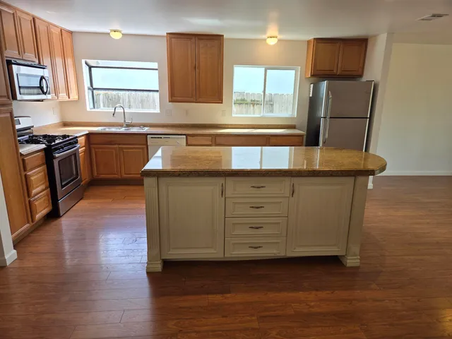 a kitchen with stainless steel appliances granite countertop a sink a stove a refrigerator with grey cabinets and wooden floor