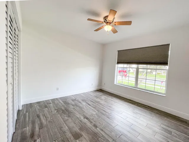 an empty room with wooden floor fan and windows