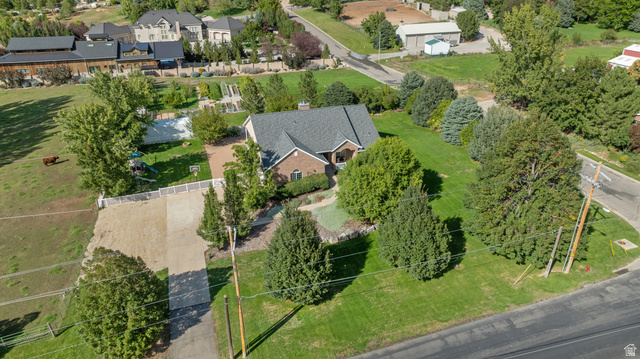 Brick exterior residence with a dark shingle roof, extensive green lawn, mature trees, and a gravel driveway