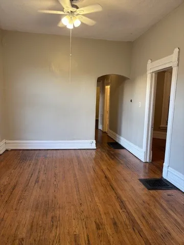 a view of an empty room with wooden floor and a ceiling fan