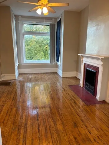 a view of an empty room with wooden floor fireplace and a window