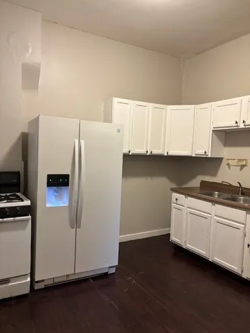 a kitchen with granite countertop a refrigerator a sink and white cabinets