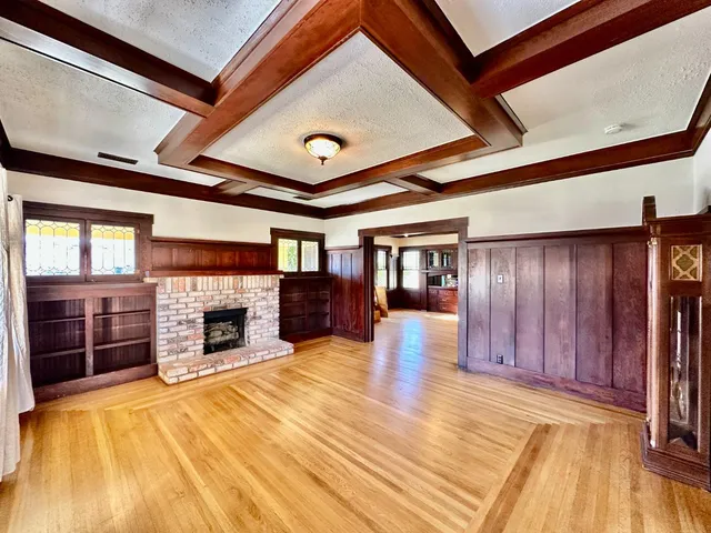 a view of an empty room with wooden floor fireplace and a window