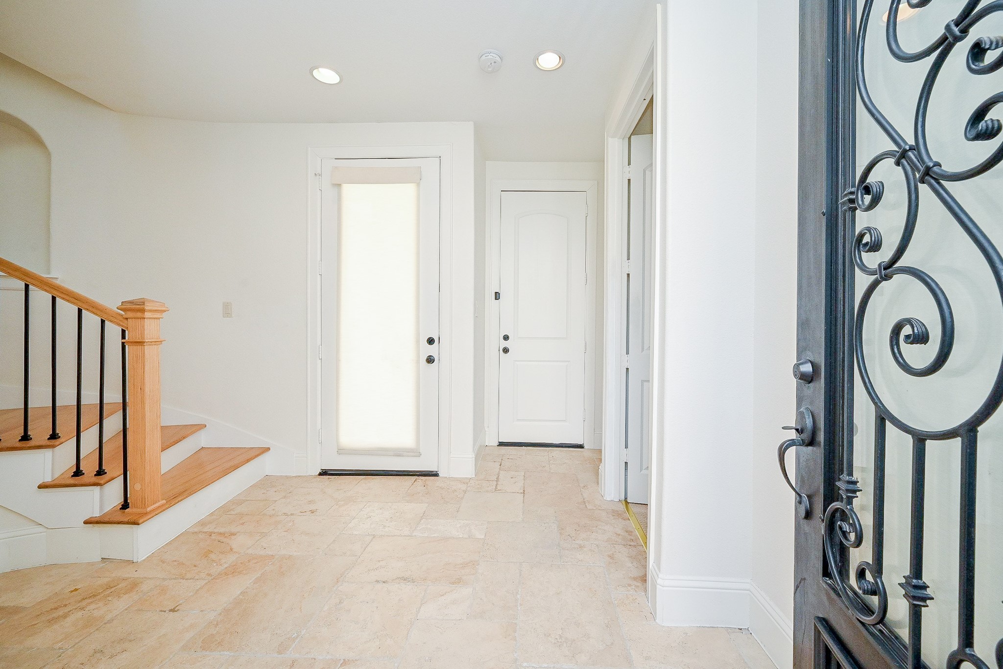 1825 West 24th Street Houston, TX 77008 - Photo 7 of 32 Bright entryway with elegant iron door, light tile flooring, and a wooden staircase with black railings. The space is inviting and well-lit, offering a warm welcome.