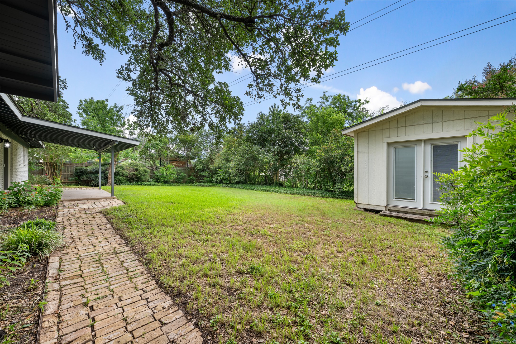 4602 Frontier Trail Austin, TX 78745 - Photo 18 of 21 A well-maintained brick pathway leads to a shaded patio, perfect for enjoying the spacious yard and detached storage building.