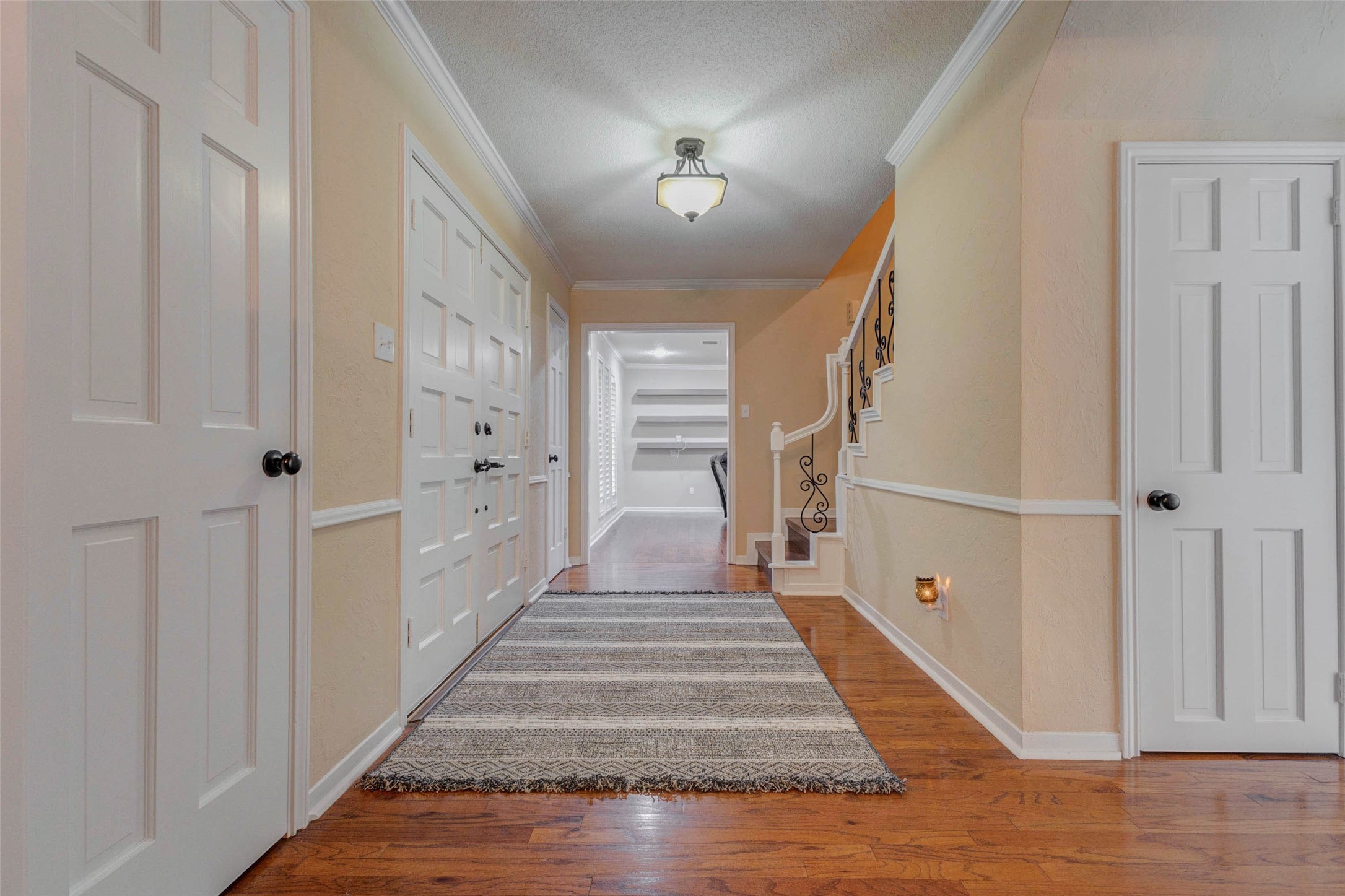 6710 Falling Waters Drive Spring, TX 77379 - Photo 7 of 46 This inviting hallway features warm wood flooring, soft beige walls, and a stylish central light fixture. It includes a large double-door entry and a staircase with elegant wrought-iron details.