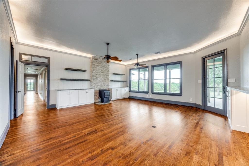 3244 Joe Davis Road Whitewright, TX 75491 - Photo 8 of 28 Unfurnished living room featuring a wood stove, a ceiling fan, ornamental molding, wood finished floors, and healthy amount of natural light