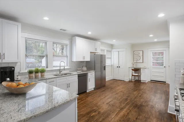 a kitchen with stainless steel appliances granite countertop a stove top oven a sink dishwasher and white cabinets with wooden floor