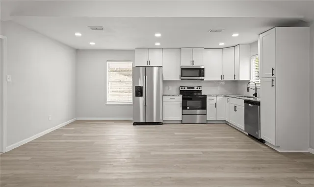 a kitchen with stainless steel appliances kitchen island granite countertop a stove top oven a refrigerator and white cabinets with wooden floor