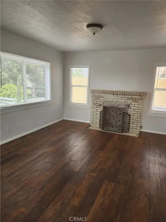 an empty room with wooden floor fireplace and windows