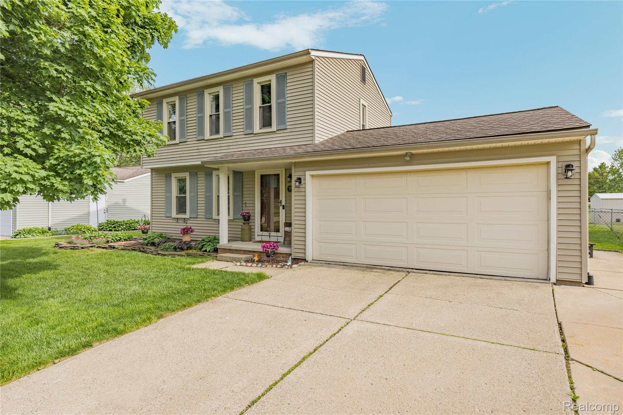 3553 Loon Lake Road Wixom, MI 48393 - Photo 2 of 25 Two-story residential exterior featuring light-colored siding, a two-car garage, concrete driveway, and front entryway with a porch