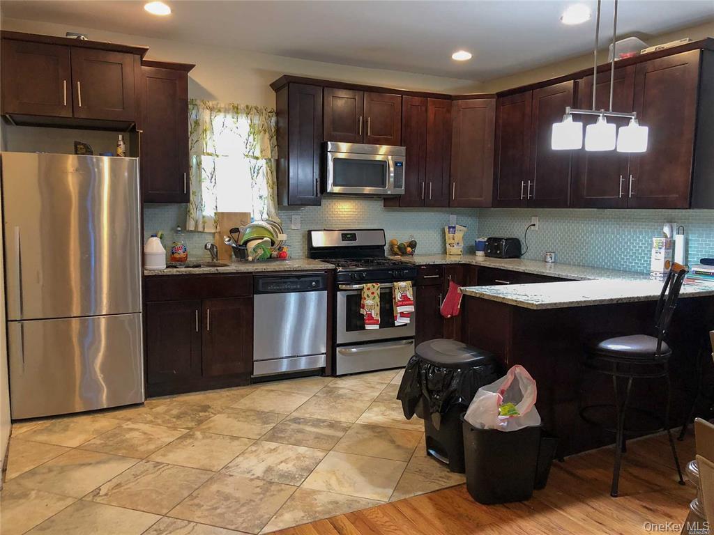 216-21 133rd Road Queens, NY 11413 - Photo 4 of 5 Kitchen featuring appliances with stainless steel finishes, dark brown cabinets, decorative backsplash, light stone countertops, and pendant lighting