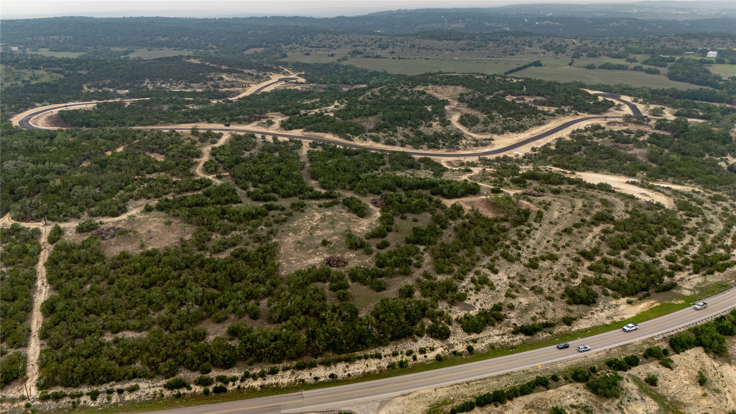 Lot 5 Ranch Road 165 Dripping Springs, TX 78620 - Photo 7 of 12 Expansive undeveloped land featuring a paved roadway, existing highway frontage, and dense natural foliage