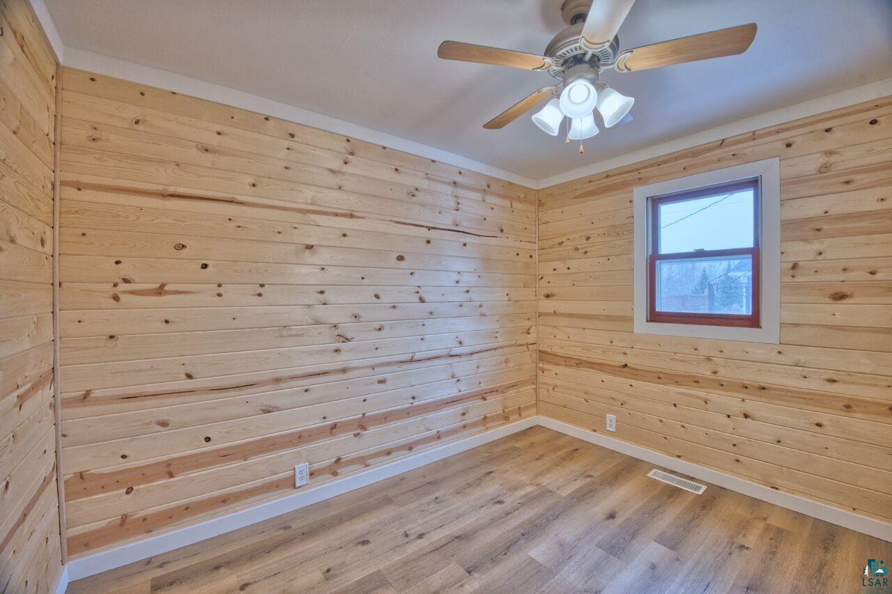 802 3rd Street Northwest Chisholm, MN 55719 - Photo 13 of 51 Unfurnished room with wood finished floors, wooden walls, ornamental molding, and a ceiling fan