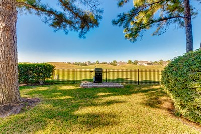 16434 Redcrest Drive Houston, TX 77095 - Photo 31 of 44 This photo showcases a serene backyard with a well-maintained lawn, bordered by trees and shrubs. A black fence offers a view of expansive open golf course under a clear blue sky, creating a peaceful outdoor space.
