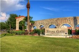 16434 Redcrest Drive Houston, TX 77095 - Photo 34 of 44 This photo showcases the entrance to the Stone Gate community, featuring a stone wall with arches, a palm tree, and well-maintained landscaping under a clear blue sky.