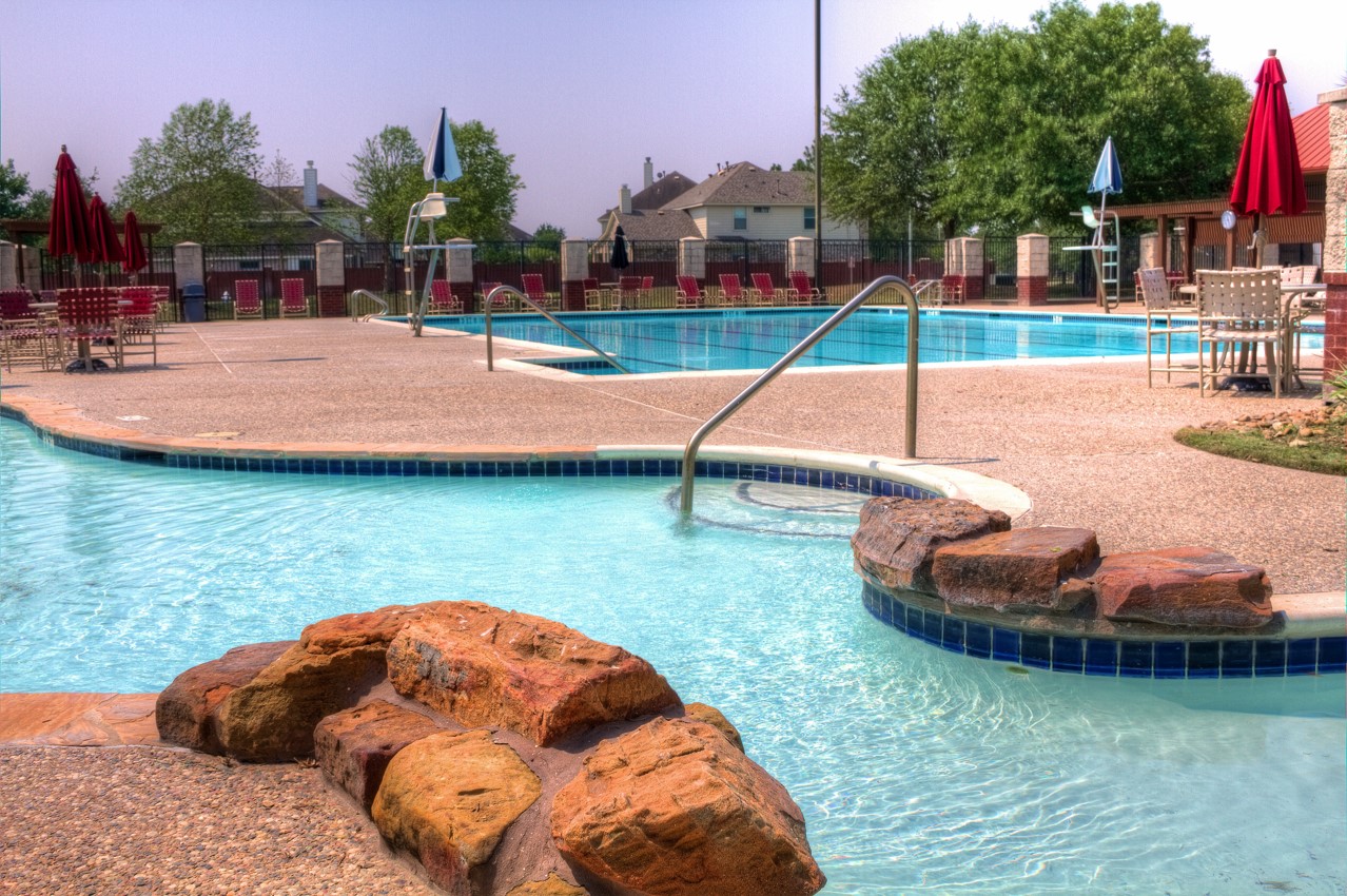 16434 Redcrest Drive Houston, TX 77095 - Photo 37 of 44 This photo showcases a spacious community pool area with a natural stone feature and ample seating under umbrellas, ideal for relaxation and gatherings.