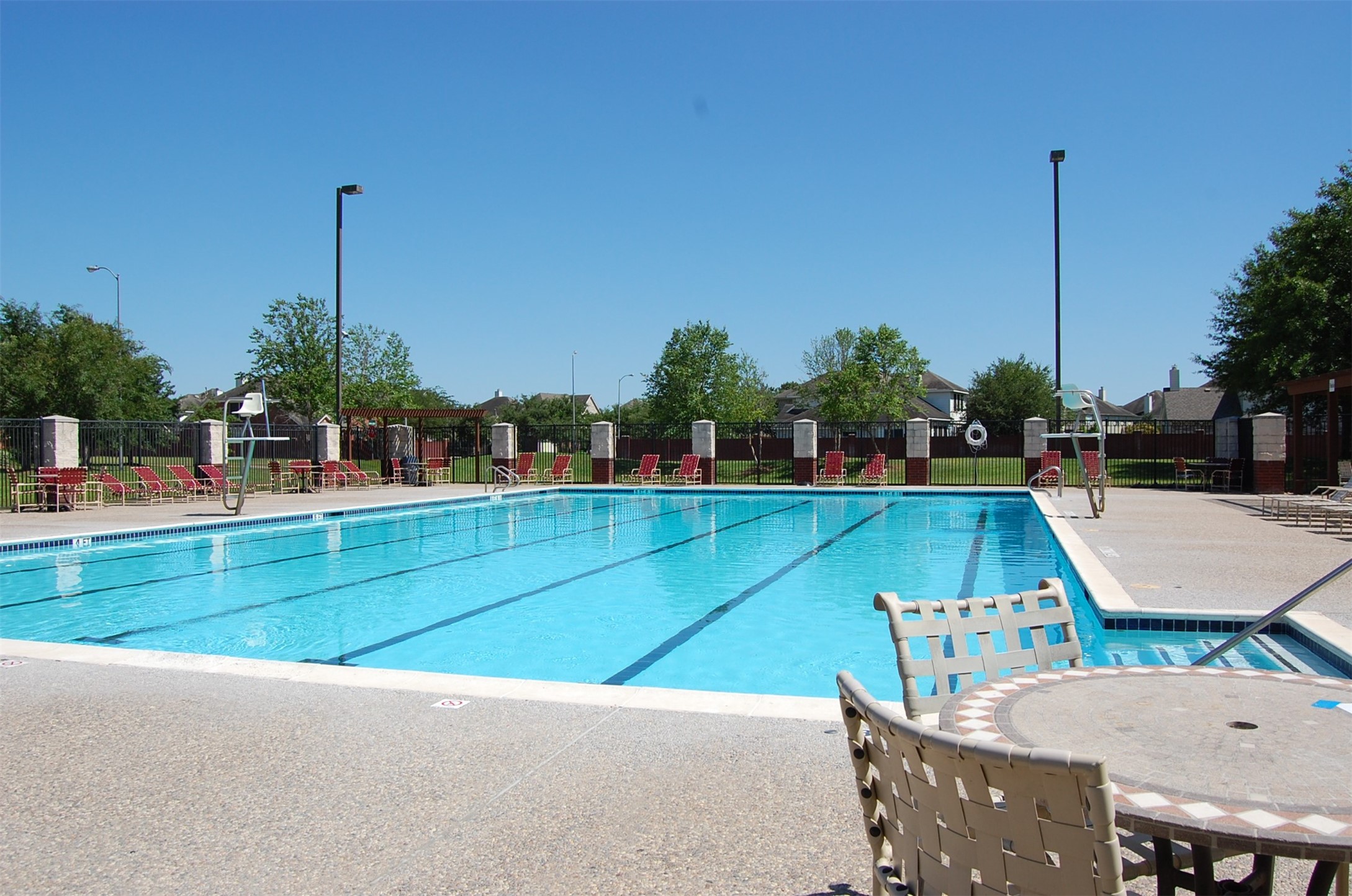 16434 Redcrest Drive Houston, TX 77095 - Photo 38 of 44 This photo showcases a spacious community/competition pool with clear water, surrounded by red lounge chairs and tables. The area is fenced, with green lawns and trees in the background, providing a relaxing outdoor environment. Less than a block from the house.