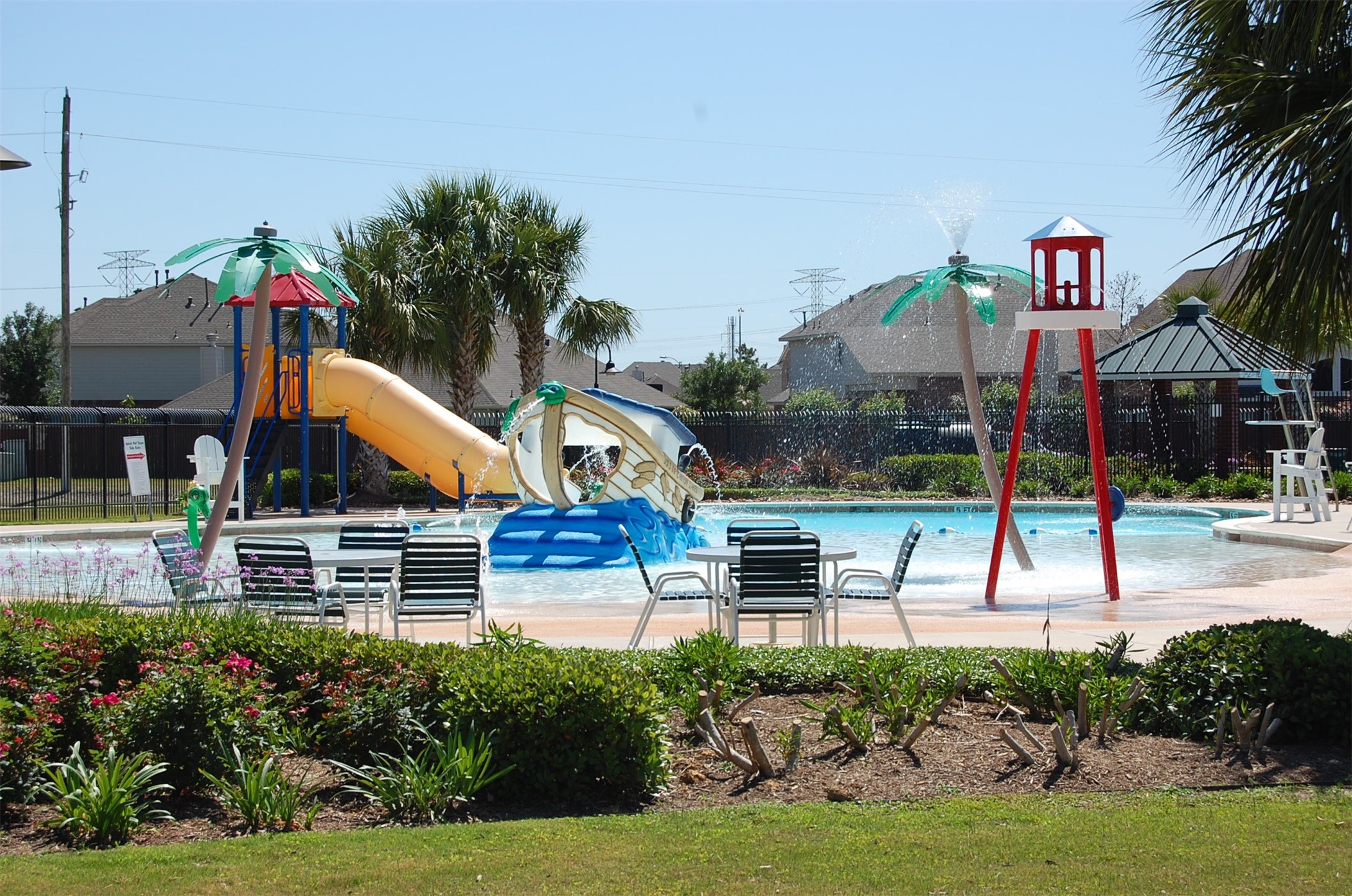 16434 Redcrest Drive Houston, TX 77095 - Photo 39 of 44 This photo showcases a family-friendly community pool area with a fun water play structure, slides, and splash features. The space is surrounded by well-maintained landscaping, providing a pleasant and inviting atmosphere for relaxation and recreation.