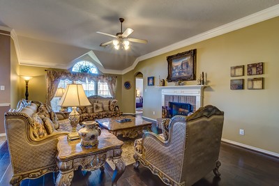 16434 Redcrest Drive Houston, TX 77095 - Photo 7 of 44 This elegant living room features high ceilings with a ceiling fan, large arched windows for natural light, and a cozy fireplace and has warm, neutral walls and dark hardwood floors, creating a welcoming and sophisticated atmosphere.