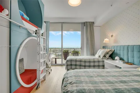 a bedroom with a bed a table chair and large windows
