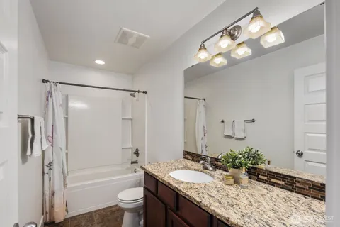 a bathroom with a granite countertop sink a toilet a mirror a vanity and shower