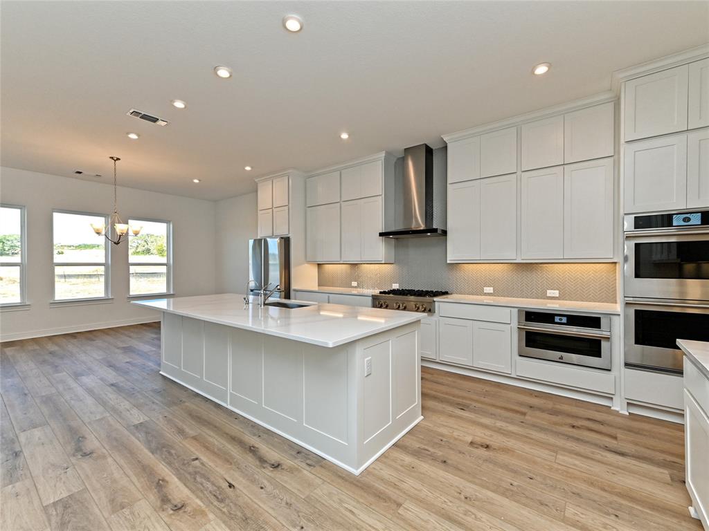 270 Prairie Clover Drive Dripping Springs, TX 78620 - Photo 11 of 28 Kitchen with stainless steel appliances, backsplash, hanging lights, white cabinets, and a kitchen island with sink