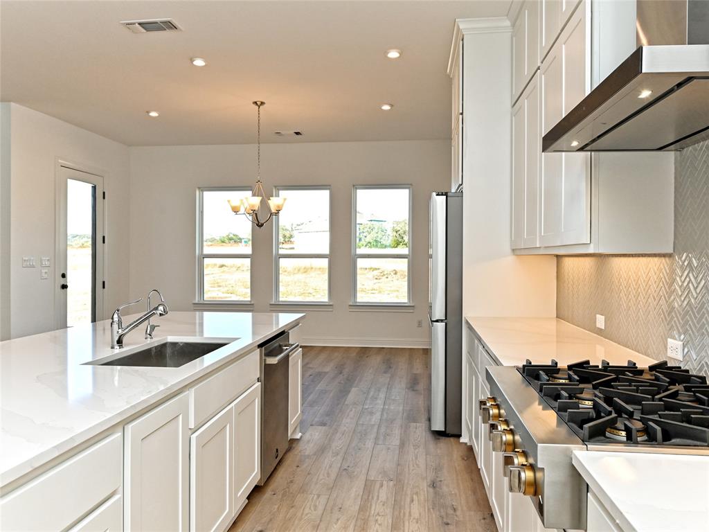 270 Prairie Clover Drive Dripping Springs, TX 78620 - Photo 12 of 28 Kitchen with white cabinetry, stainless steel appliances, light wood-style flooring, a chandelier, and light stone countertops