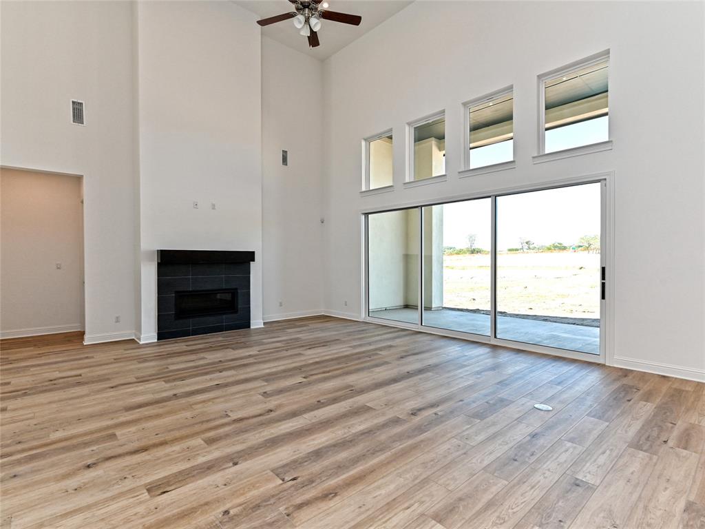 270 Prairie Clover Drive Dripping Springs, TX 78620 - Photo 5 of 28 Unfurnished living room with a tiled fireplace, ceiling fan, a high ceiling, and light wood-style floors
