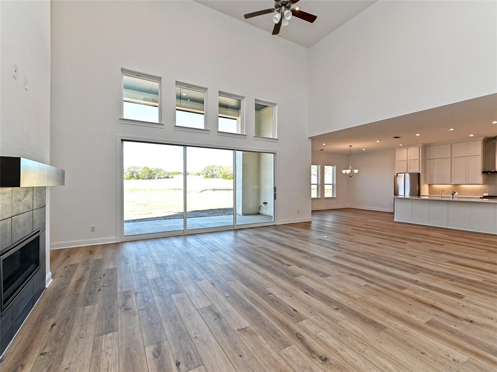 270 Prairie Clover Drive Dripping Springs, TX 78620 - Photo 6 of 28 Unfurnished living room featuring a tiled fireplace, ceiling fan, suspended lighting, light wood finished floors, and a high ceiling