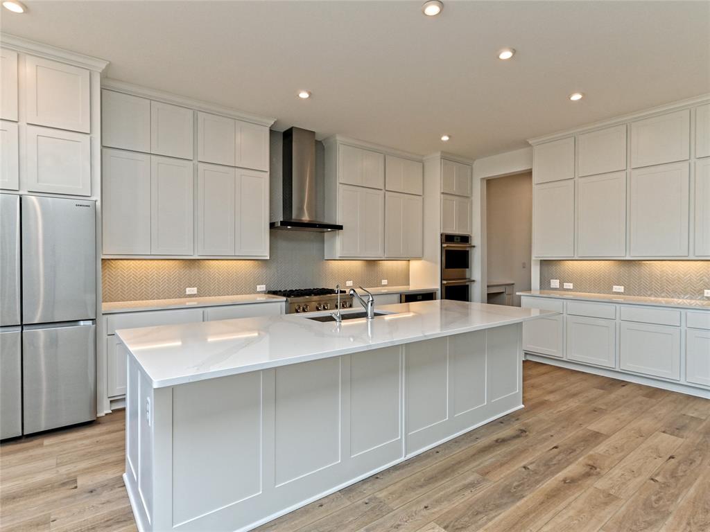 270 Prairie Clover Drive Dripping Springs, TX 78620 - Photo 10 of 28 Kitchen featuring stainless steel appliances, light wood finished floors, light stone counters, recessed lighting, and a spacious island