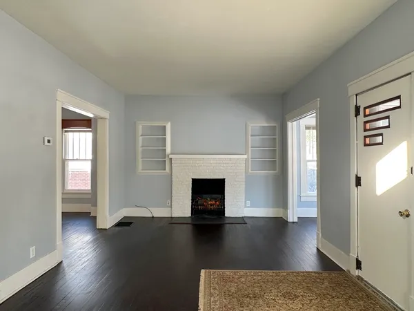an empty room with wooden floor fireplace and windows