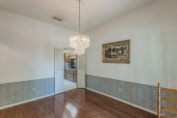 an empty room with wooden floor chandelier and entryway