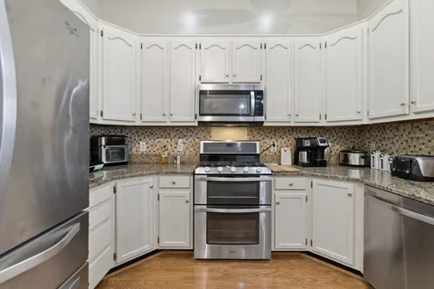 a kitchen with stainless steel appliances granite countertop a stove a sink and white cabinets