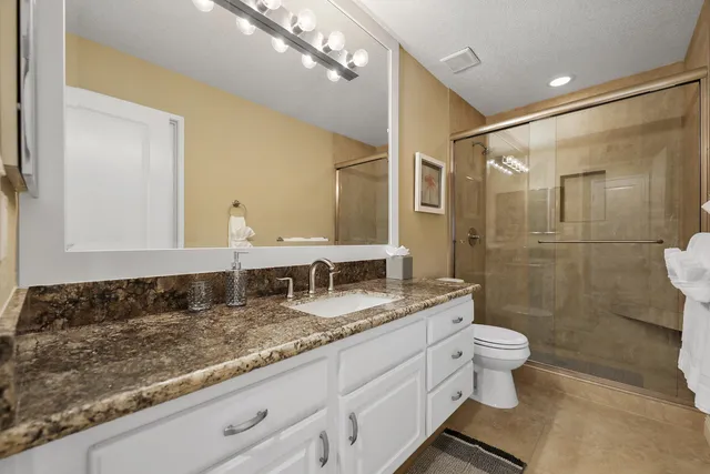 a bathroom with a granite countertop sink a toilet a mirror and shower