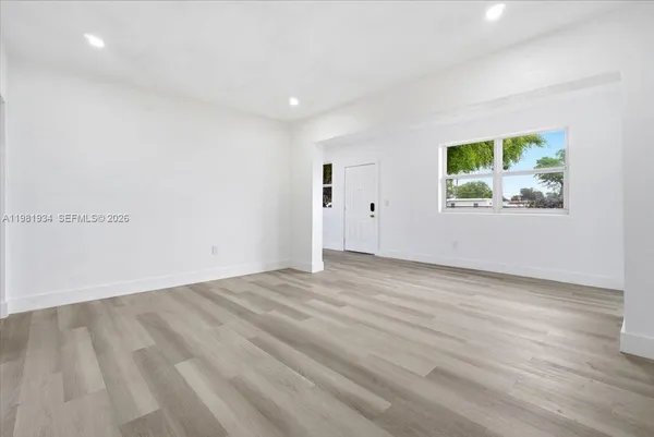 a view of an empty room with wooden floor and a window