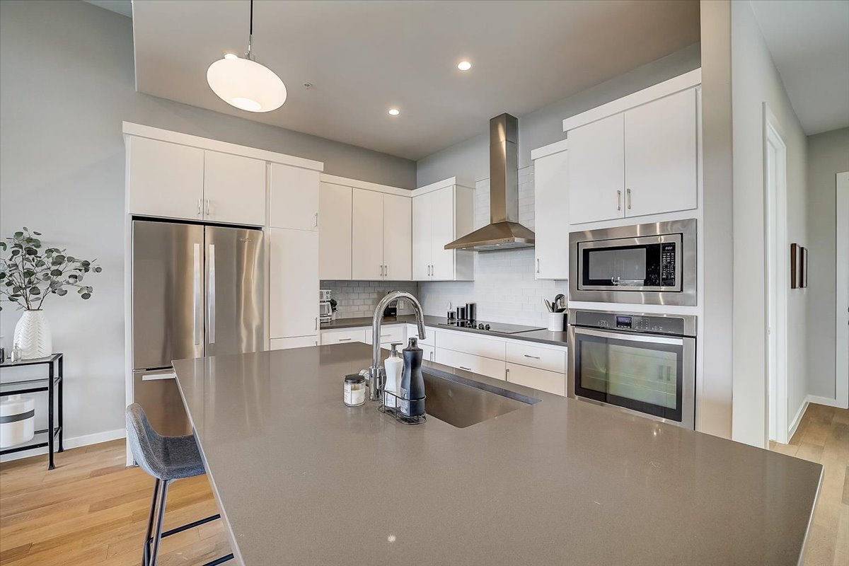 5921 Hiline Road, Unit 1204 Austin, TX 78734 - Photo 13 of 36 Kitchen with decorative light fixtures, appliances with stainless steel finishes, wall chimney range hood, white cabinetry, and tasteful backsplash