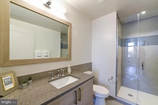 a bathroom with a granite countertop sink a toilet a mirror and shower