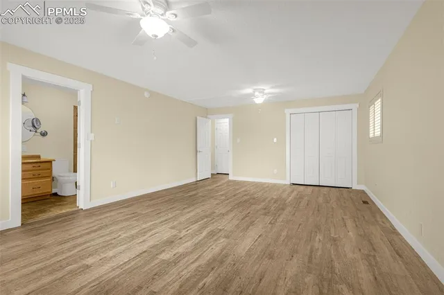 a view of an empty room with wooden floor and a ceiling fan
