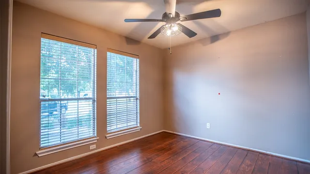 an empty room with wooden floor fan and windows