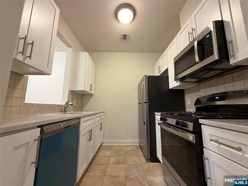 a kitchen with stainless steel appliances a sink a stove a microwave a refrigerator a sink and cabinets