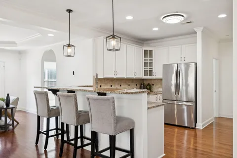 a kitchen with stainless steel appliances granite countertop a refrigerator a stove a sink dishwasher and white cabinets with wooden floor