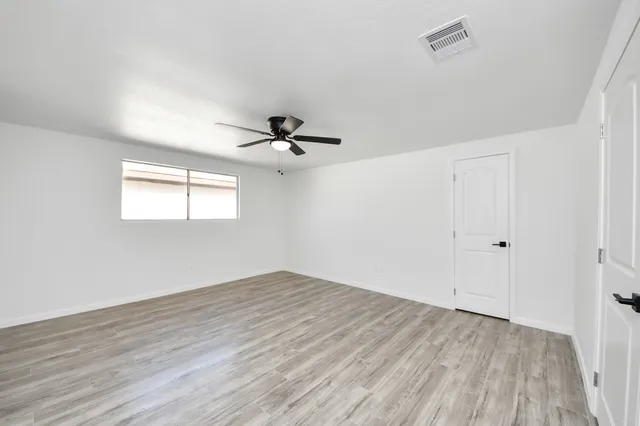 an empty room with wooden floor fan and windows