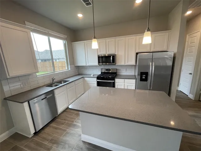 a large kitchen with stainless steel appliances a refrigerator a sink a stove a microwave a center island and furniture