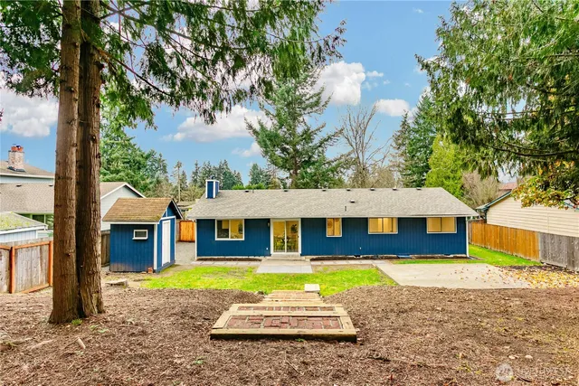 a view of a white house with a large tree and a yard with lawn chairs