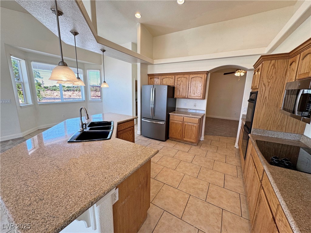 1771 Labrador Street Pahrump, NV 89048 - Photo 23 of 64 Kitchen with stainless steel appliances, a kitchen island with sink, brown cabinetry, light tile patterned flooring, and hanging light fixtures